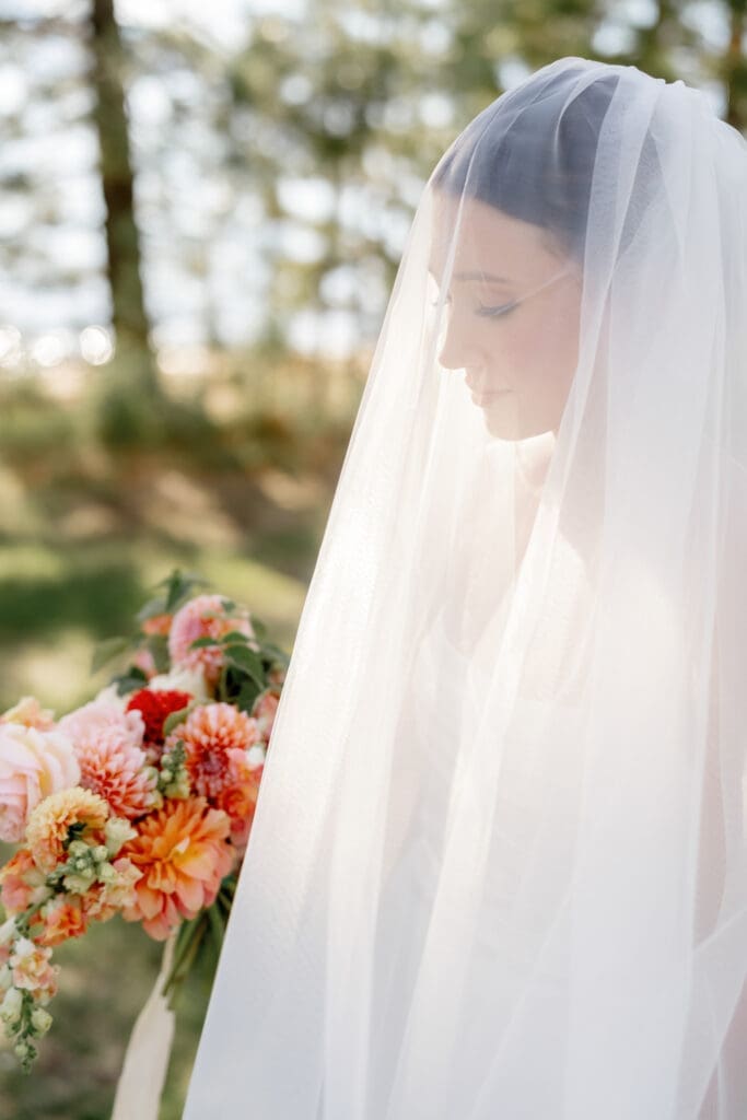 Bride wearing a sheer wedding veil and holding a colorful floral bouquet during an outdoor Lake Tahoe wedding.