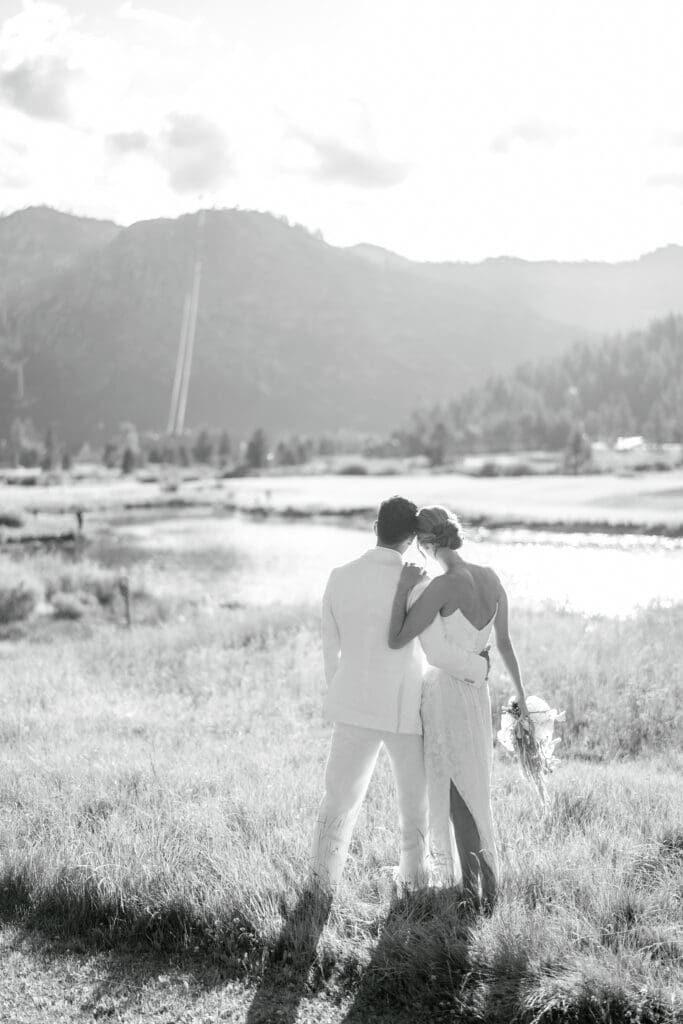 Black-and-white photograph of newlyweds embracing in a meadow surrounded by the Sierra Nevada mountains during an Everline Resort & Spa wedding.