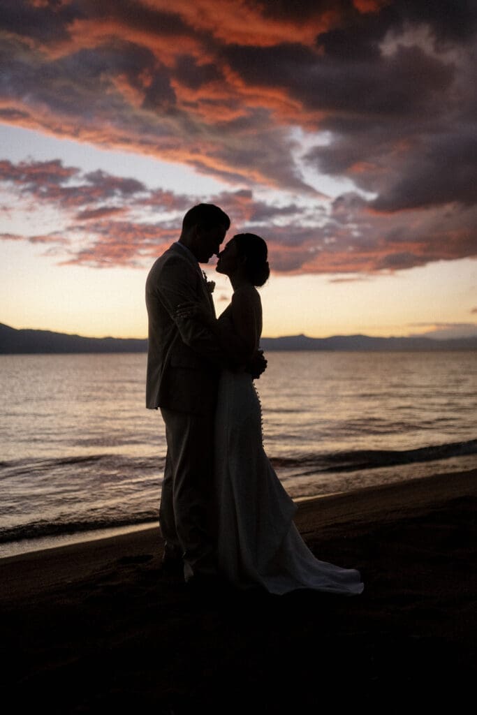 Bride and groom silhouetted against a colorful Lake Tahoe sunset during evening portraits.
