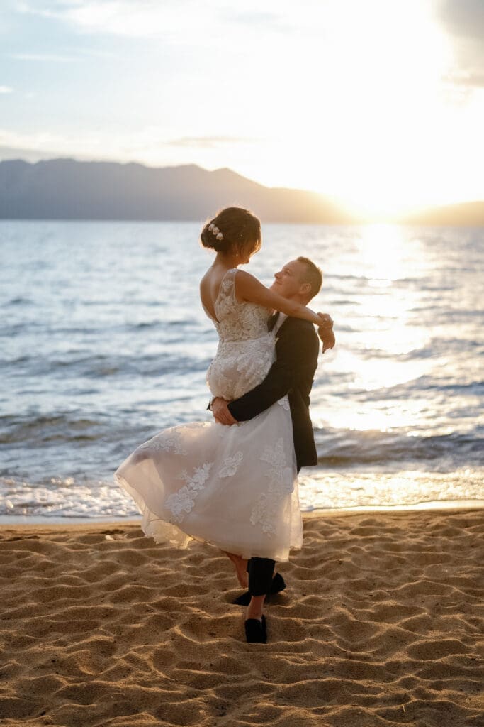 Groom carrying bride along the beach at sunset on the shores of Lake Tahoe.