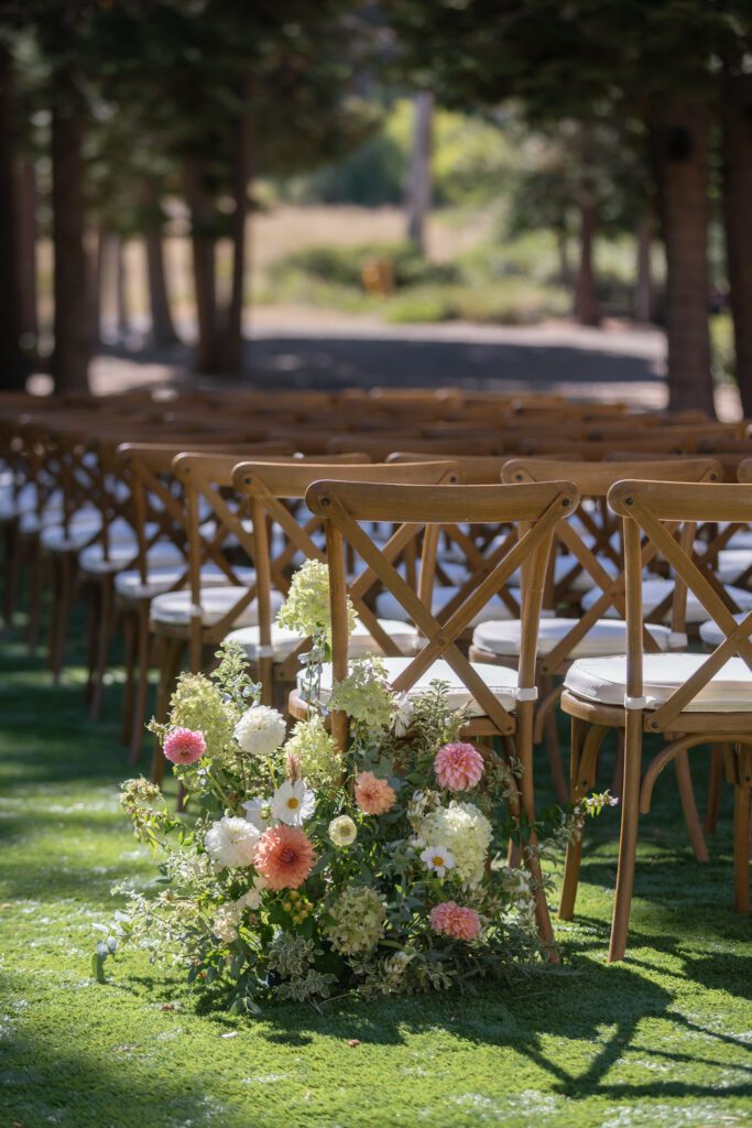 Outdoor wedding ceremony at The Ritz-Carlton Lake Tahoe featuring wooden guest chairs and colorful floral arrangements beneath pine trees.