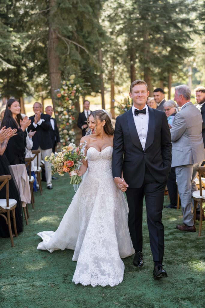Newlyweds walking hand in hand down a forest wedding aisle as guests applaud during a Ritz-Carlton Lake Tahoe wedding.