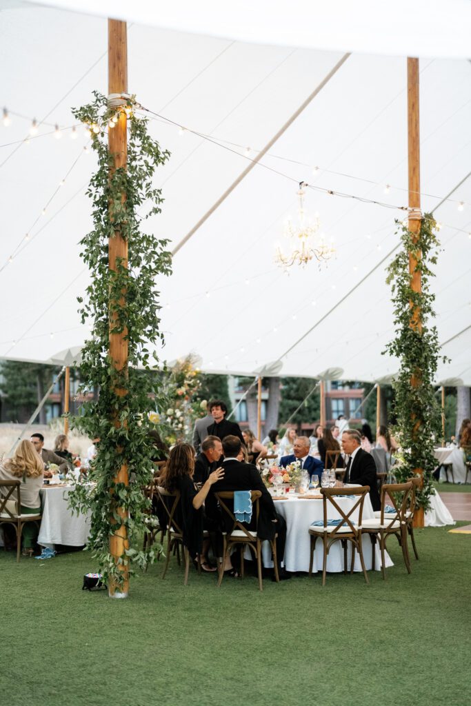 Elegant tented wedding reception featuring white linens, hanging greenery, chandeliers, and round dining tables at a mountain resort.