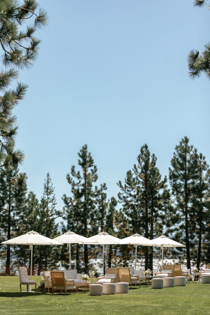 Luxury outdoor cocktail lounge at Edgewood Tahoe featuring white umbrellas, neutral seating, and towering pine trees on a manicured lawn.