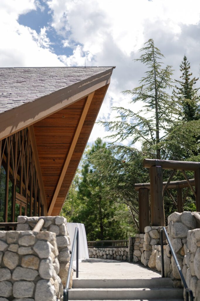 Edgewood Tahoe wedding venue featuring rustic stone architecture, natural wood beams, and towering pine trees beneath a blue sky.