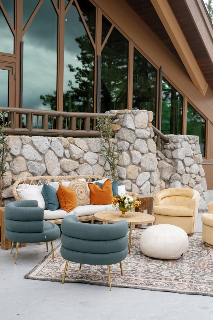 Elegant outdoor wedding lounge at Edgewood Tahoe featuring blue upholstered chairs, neutral sofas, and warm floral accents beside stone architecture.