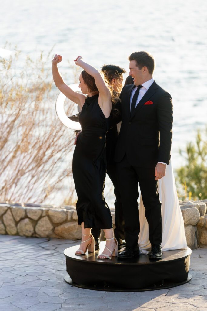Elegantly dressed wedding guests celebrating together on a raised platform beside Lake Tahoe during a formal wedding reception.
