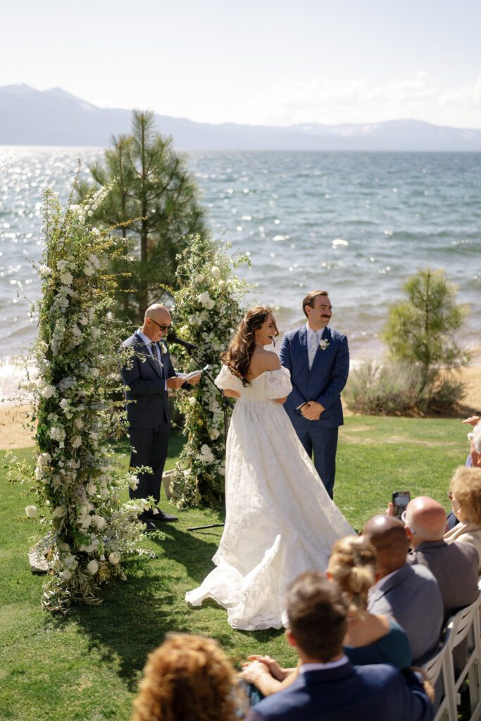 Edgewood Tahoe wedding ceremony overlooking Lake Tahoe as a bride and groom exchange vows surrounded by guests and floral arrangements.