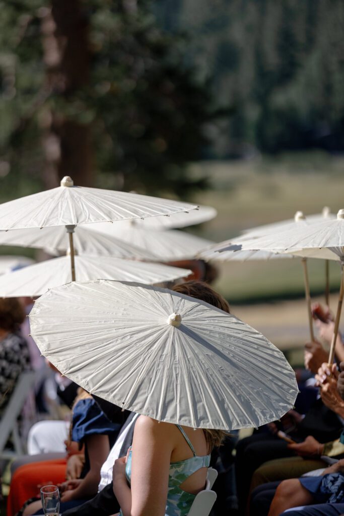 White parasols shading wedding guests during an outdoor ceremony surrounded by mountain scenery in Olympic Valley.