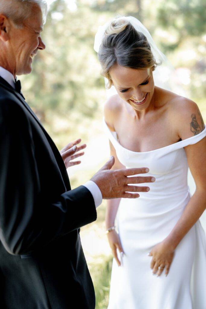 Bride wearing an off-the-shoulder white wedding gown sharing a joyful moment with an older gentleman during an outdoor celebration.