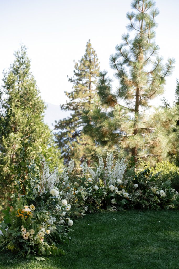 Lush garden-style wedding floral arrangements surrounded by towering pine trees at a Glenbrook Lake Tahoe wedding venue.