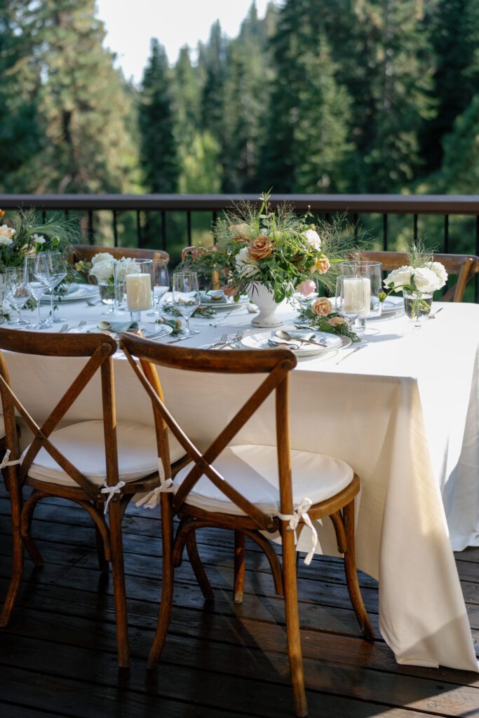 Luxury Lake Tahoe wedding venue reception featuring an elegant tablescape with white linens, floral arrangements, and wooden chairs overlooking the forest.