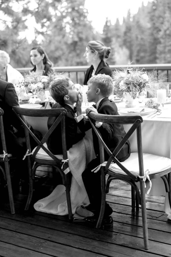 Black-and-white photograph of wedding guests seated at an elegant outdoor reception table surrounded by mountain scenery.