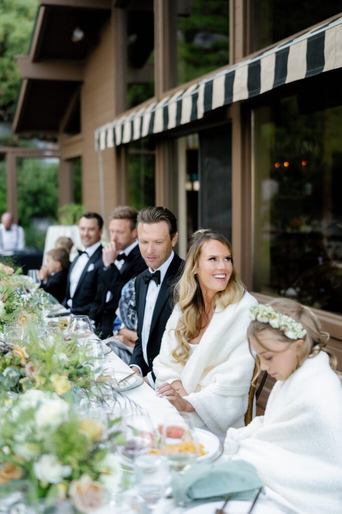 Bride and wedding guests enjoying an elegant outdoor reception with floral centerpieces and mountain lodge architecture.