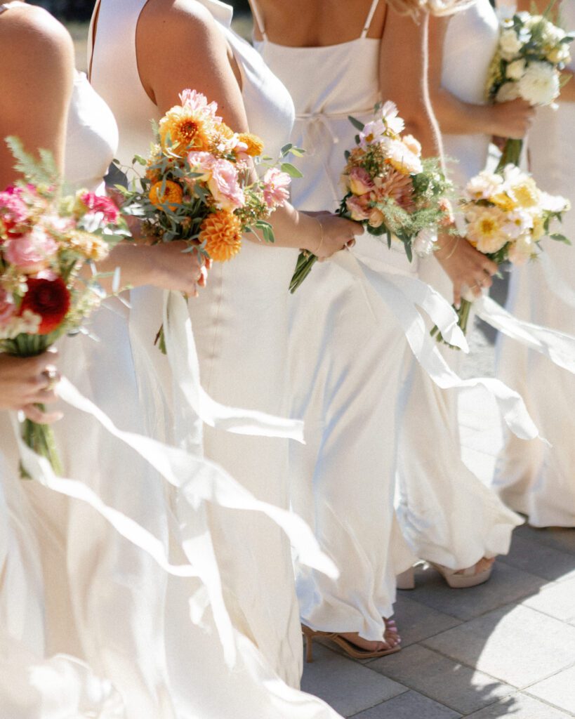 Bridesmaids wearing ivory dresses and holding colorful bouquets of orange, pink, and peach flowers during a Lake Tahoe wedding celebration.