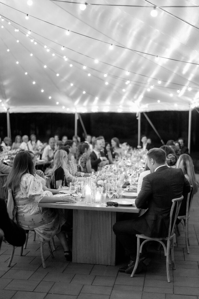 Black-and-white photograph of an elegant tented Lake Tahoe wedding reception with string lights and guests gathered around long dining tables.