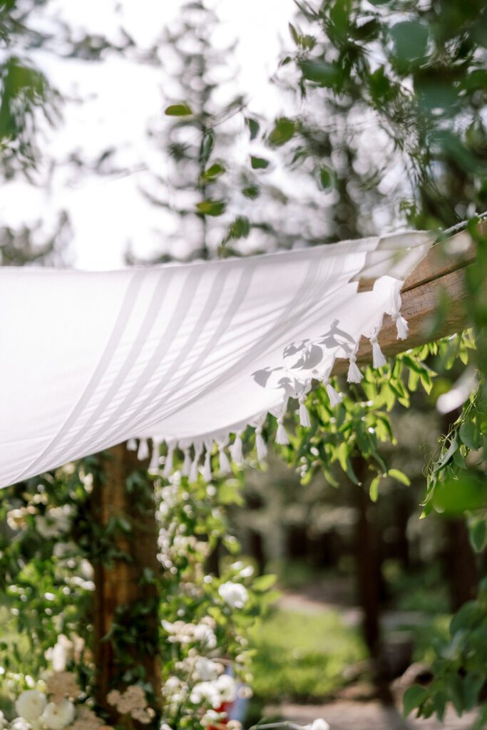 White draped fabric and delicate greenery creating a romantic outdoor wedding ceremony setting beneath the trees.